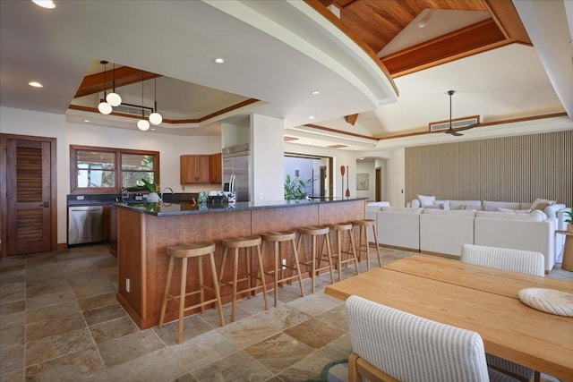 kitchen featuring decorative light fixtures, a raised ceiling, a breakfast bar, and appliances with stainless steel finishes