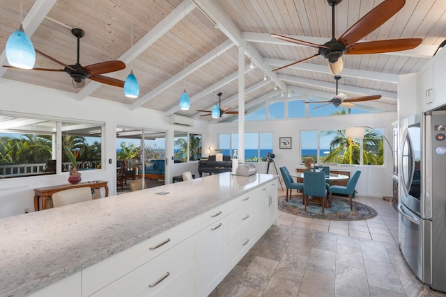 kitchen featuring white cabinetry, stainless steel fridge, a wall unit AC, light stone countertops, and beam ceiling