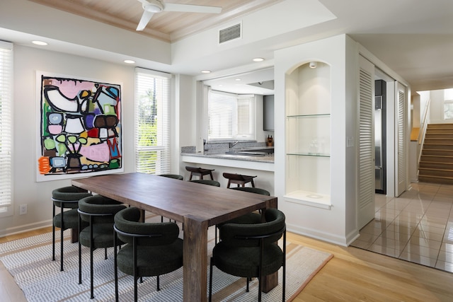 dining area with ornamental molding, ceiling fan, a tray ceiling, light wood-type flooring, and built in shelves