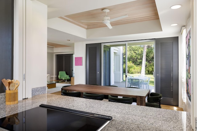 kitchen featuring a tray ceiling, ornamental molding, light stone countertops, and ceiling fan