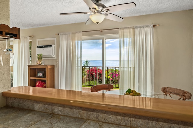 dining space with ceiling fan, a textured ceiling, a wall unit AC, and a water view