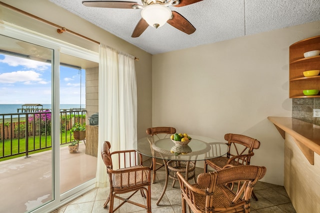 tiled dining room featuring ceiling fan, a textured ceiling, and a water view