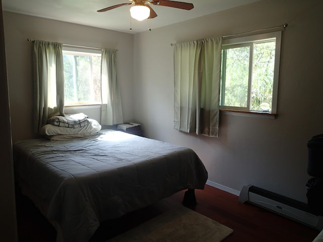 bedroom with ceiling fan, wood-type flooring, and a baseboard heating unit