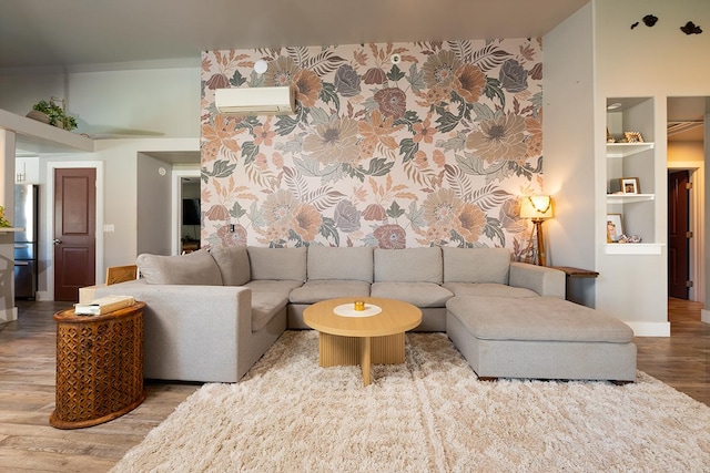 living room with an AC wall unit, built in features, and wood-type flooring