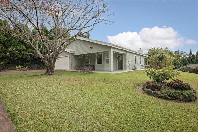 rear view of property featuring a garage, a patio area, and a lawn