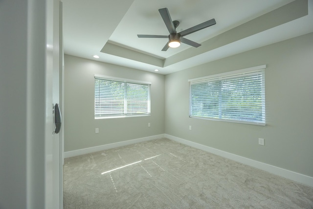 empty room with a raised ceiling, light colored carpet, and ceiling fan