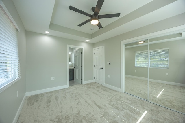 unfurnished bedroom with ceiling fan, a closet, connected bathroom, and a raised ceiling