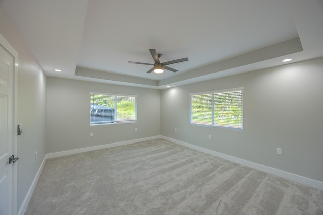 carpeted spare room featuring ceiling fan, plenty of natural light, and a tray ceiling