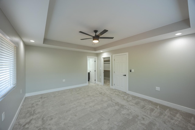 spare room featuring ceiling fan, a tray ceiling, and light carpet