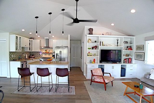 kitchen with stainless steel refrigerator with ice dispenser, lofted ceiling, wall chimney range hood, white cabinets, and a center island