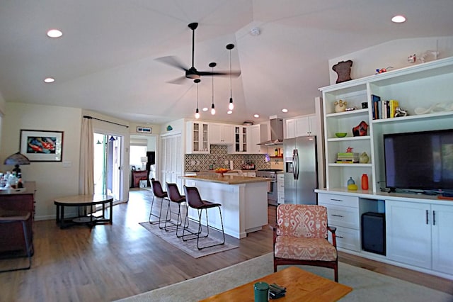 kitchen featuring lofted ceiling, wall chimney range hood, white cabinetry, a breakfast bar area, and stainless steel appliances