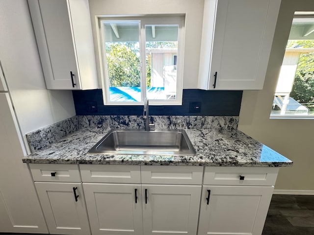 kitchen with light stone countertops, white cabinetry, dark wood-type flooring, and sink