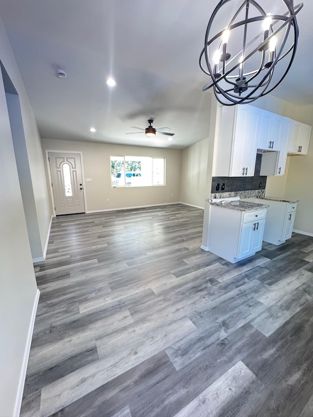 kitchen featuring backsplash, ceiling fan with notable chandelier, stone counters, white cabinets, and hardwood / wood-style floors