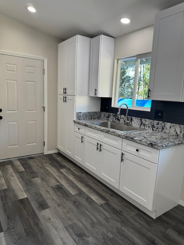 kitchen with light stone countertops, white cabinetry, sink, and dark wood-type flooring