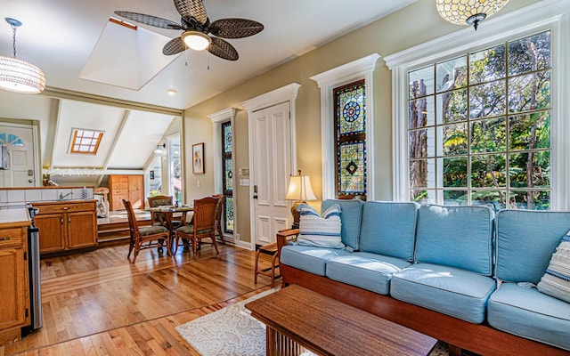 living room featuring ceiling fan, vaulted ceiling with skylight, and light wood-type flooring