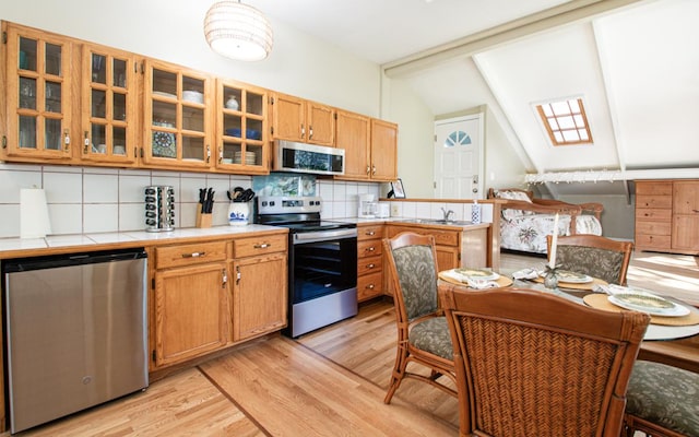 kitchen featuring tasteful backsplash, appliances with stainless steel finishes, vaulted ceiling with skylight, and light hardwood / wood-style floors