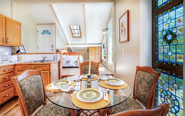 dining space featuring sink, vaulted ceiling with skylight, and light hardwood / wood-style floors