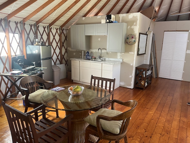 dining space with light hardwood / wood-style floors, sink, and vaulted ceiling with beams