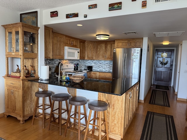 kitchen featuring backsplash, white appliances, light hardwood / wood-style floors, and kitchen peninsula