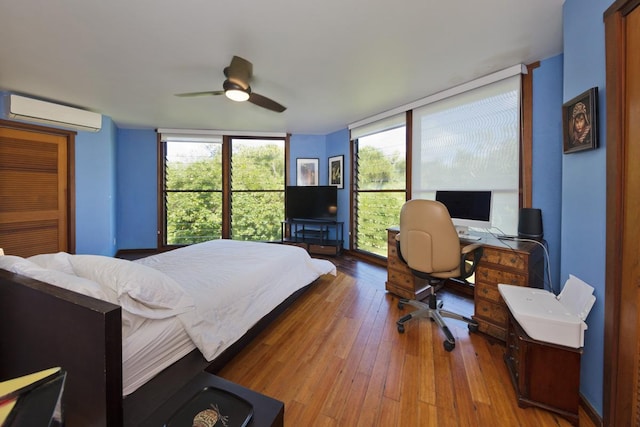 bedroom featuring ceiling fan, a wall mounted AC, multiple windows, and hardwood / wood-style flooring