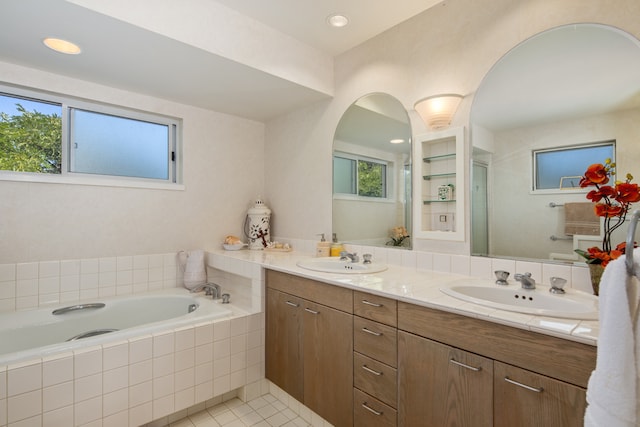 bathroom with a relaxing tiled tub, vanity, and tile patterned flooring