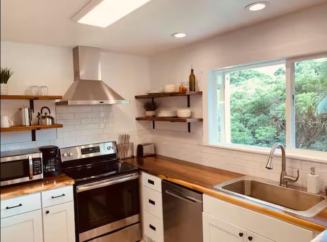 kitchen with exhaust hood, appliances with stainless steel finishes, wooden counters, and white cabinetry