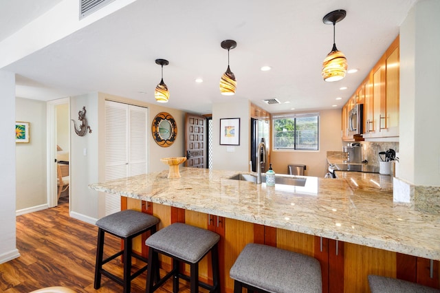 kitchen featuring sink, light stone counters, kitchen peninsula, stainless steel appliances, and dark wood-type flooring