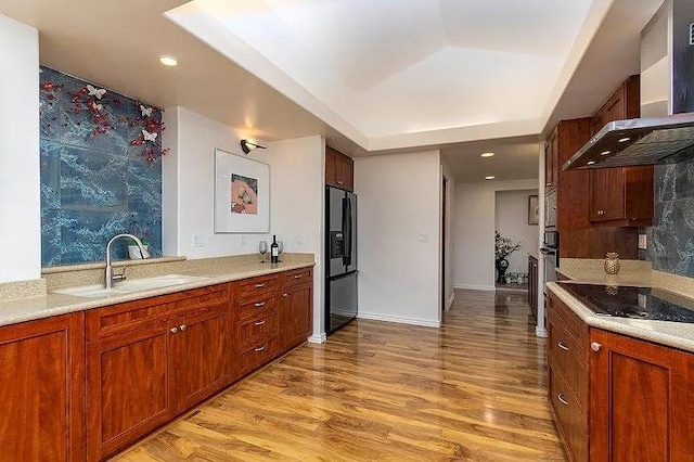 kitchen with black electric stovetop, a sink, wall chimney range hood, fridge with ice dispenser, and a raised ceiling