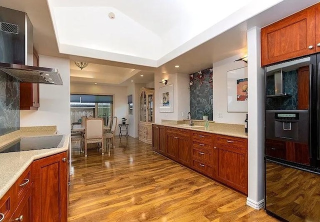 kitchen with light countertops, a tray ceiling, wall chimney exhaust hood, and a sink