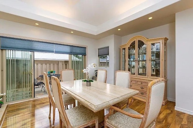 dining space featuring recessed lighting, a tray ceiling, baseboards, and wood finished floors