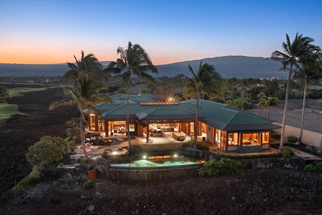 back house at dusk featuring a mountain view and a patio area