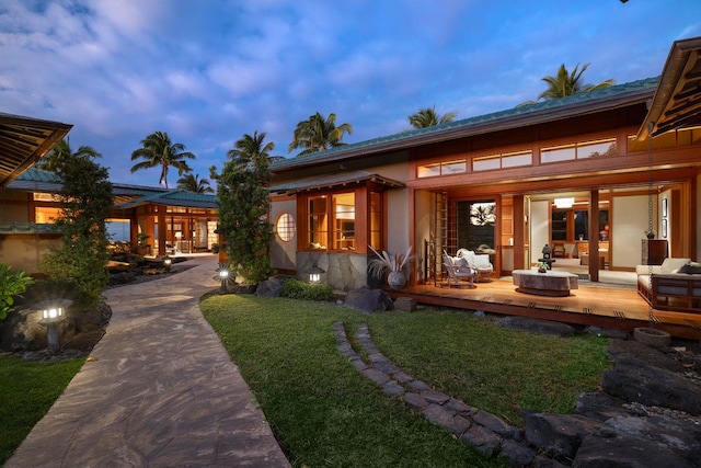 back house at dusk featuring a wooden deck and a lawn