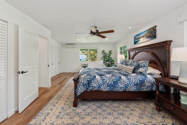 bedroom featuring a wall mounted air conditioner, light hardwood / wood-style flooring, and ceiling fan