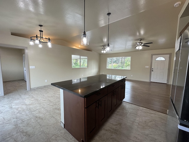 kitchen featuring ceiling fan with notable chandelier, dark brown cabinetry, lofted ceiling, a kitchen island, and decorative light fixtures