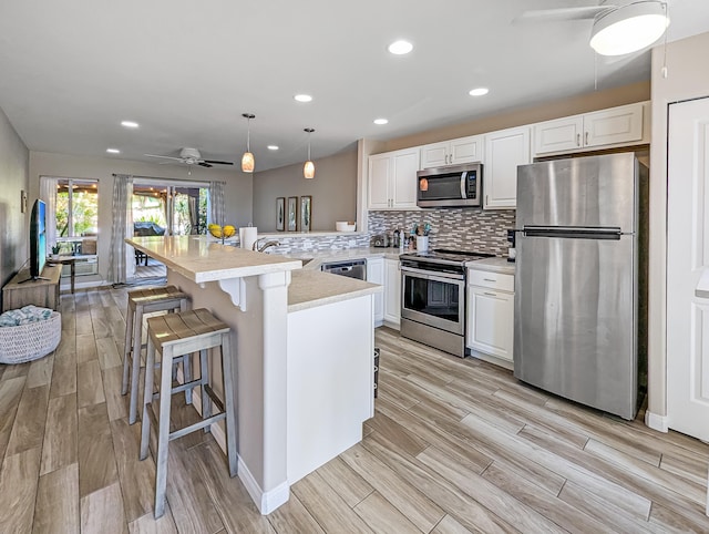 kitchen featuring pendant lighting, appliances with stainless steel finishes, backsplash, kitchen peninsula, and a breakfast bar