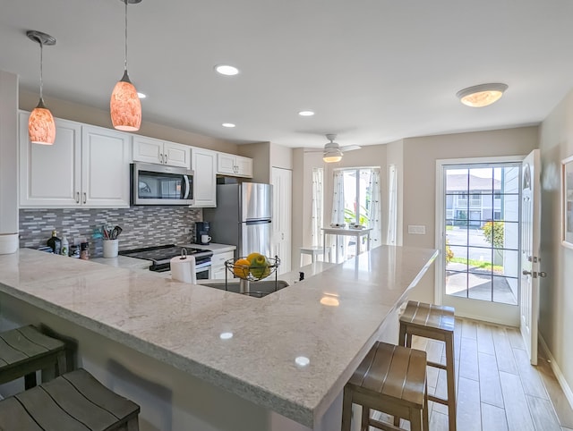 kitchen with white cabinets, a kitchen bar, stainless steel appliances, tasteful backsplash, and light stone counters