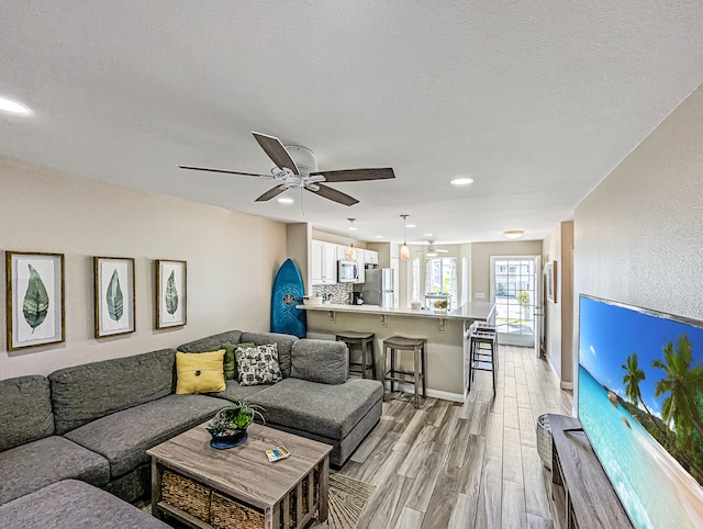 living room with light hardwood / wood-style floors, a textured ceiling, and ceiling fan