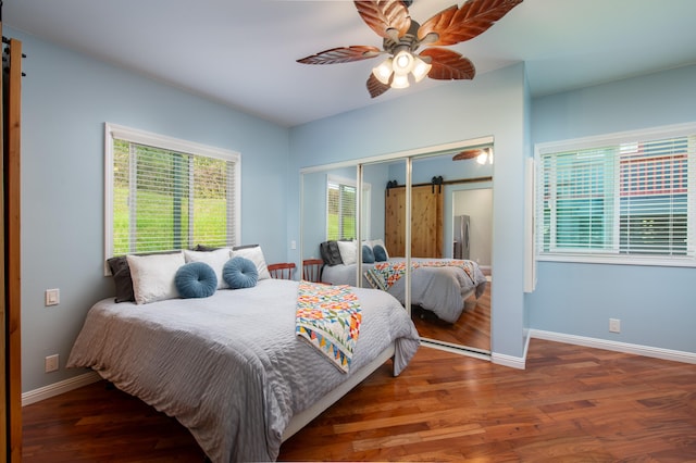 bedroom with a closet, dark hardwood / wood-style floors, a barn door, and ceiling fan