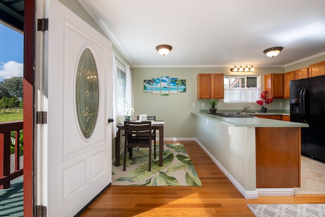 kitchen with crown molding, kitchen peninsula, black refrigerator with ice dispenser, and light wood-type flooring