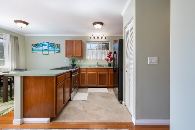 kitchen with sink, black fridge, crown molding, stainless steel range with gas cooktop, and kitchen peninsula