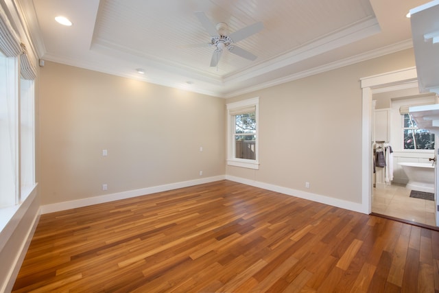 empty room featuring a raised ceiling, ceiling fan, crown molding, and light hardwood / wood-style flooring