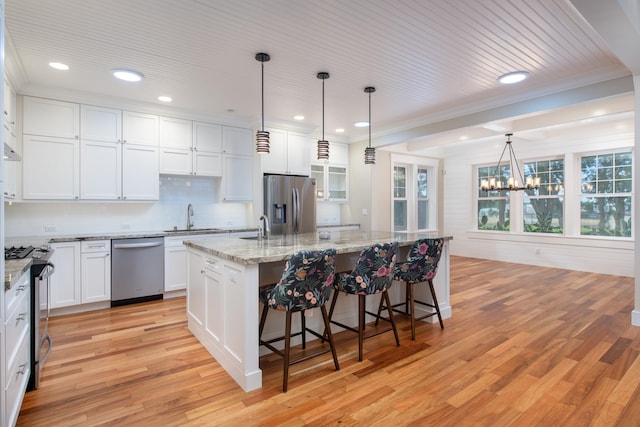 kitchen with appliances with stainless steel finishes, white cabinetry, an island with sink, sink, and hanging light fixtures