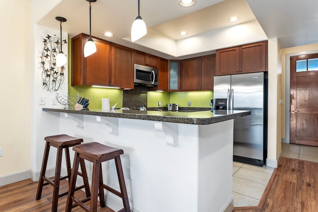 kitchen with decorative light fixtures, kitchen peninsula, light wood-type flooring, a breakfast bar area, and stainless steel appliances