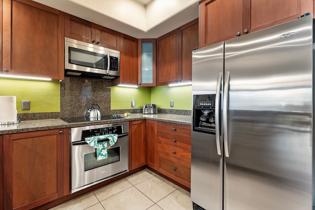 kitchen featuring tasteful backsplash, light tile patterned floors, dark stone countertops, and stainless steel appliances