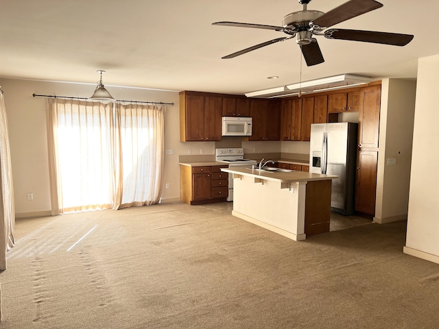 kitchen with pendant lighting, white appliances, a kitchen bar, sink, and a center island with sink