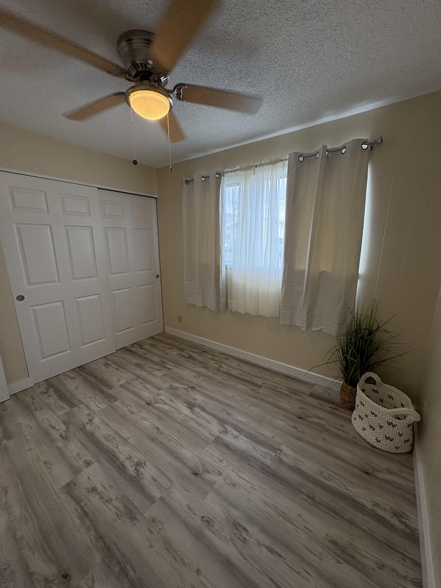 unfurnished bedroom with ceiling fan, a textured ceiling, a closet, and light wood-type flooring