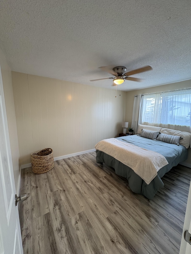 bedroom with ceiling fan, light hardwood / wood-style floors, a textured ceiling, and wood walls