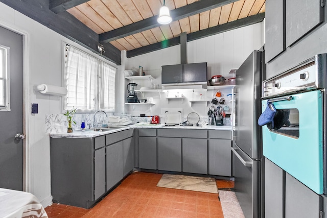 kitchen featuring oven, gray cabinets, beam ceiling, stainless steel refrigerator, and sink