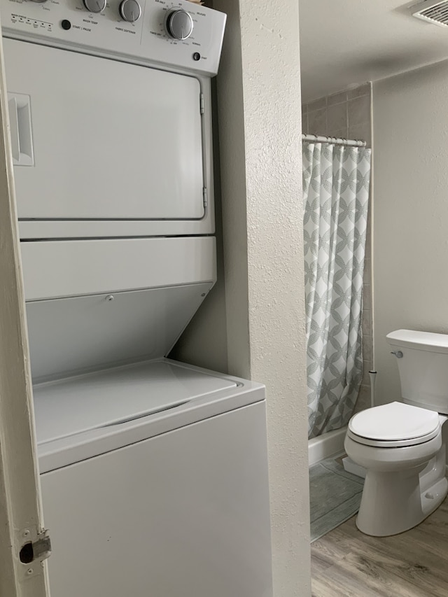 full bathroom featuring toilet, wood finished floors, stacked washer and clothes dryer, and a shower with curtain