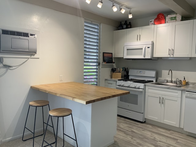 kitchen featuring white appliances, a sink, a kitchen breakfast bar, white cabinets, and wooden counters